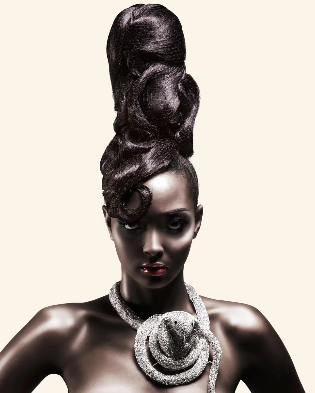 Towering sculpted updo worn with a silver snake necklace, against a cream background