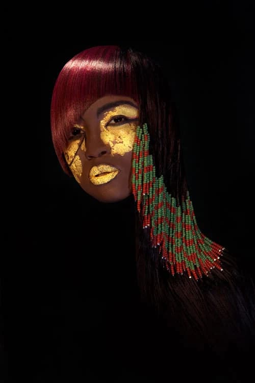 Burgundy hair with long red and green beaded strands, and gold face paint