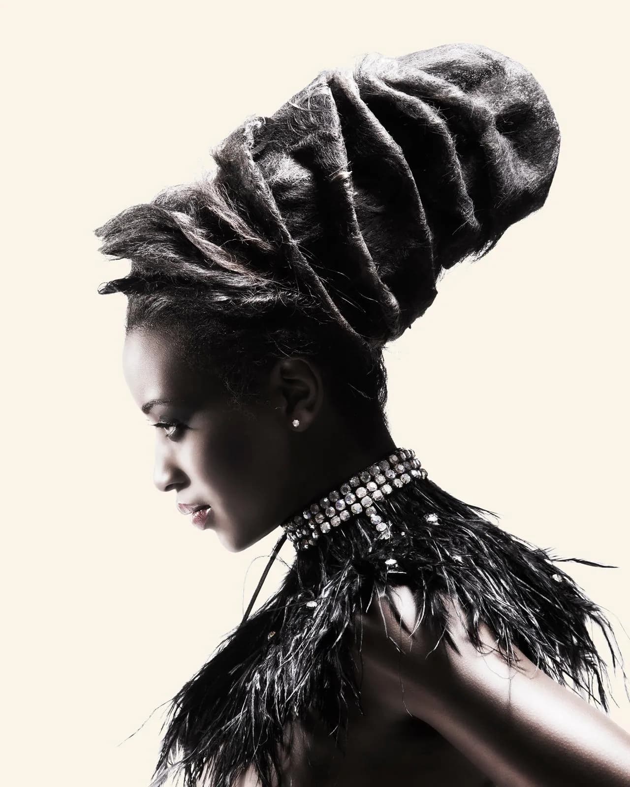 Profile of a sculpted, wrapped updo worn with a black feather collar