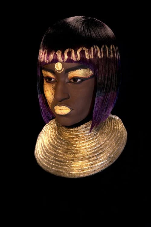 Egyptian-inspired black and purple bob with a gold headband, gold face paint and a gold collar