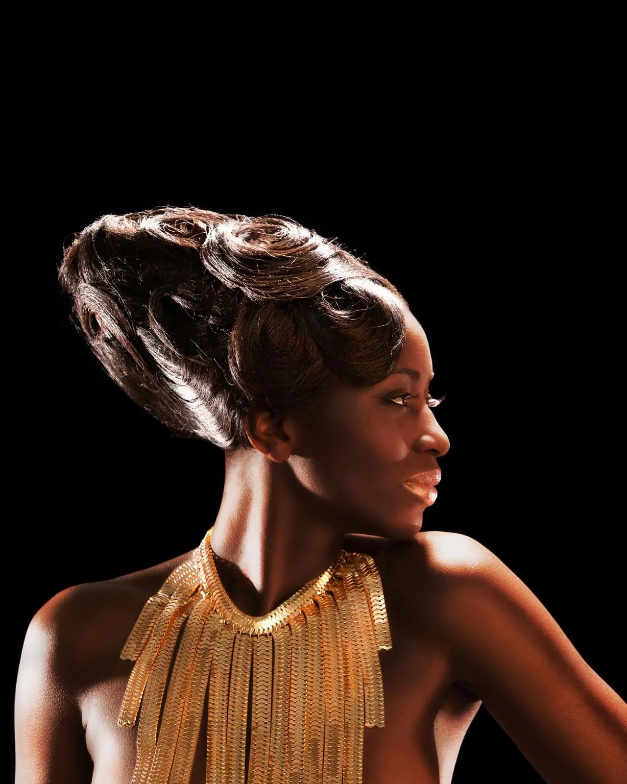 Sculpted updo in profile, finished with a gold fringed collar