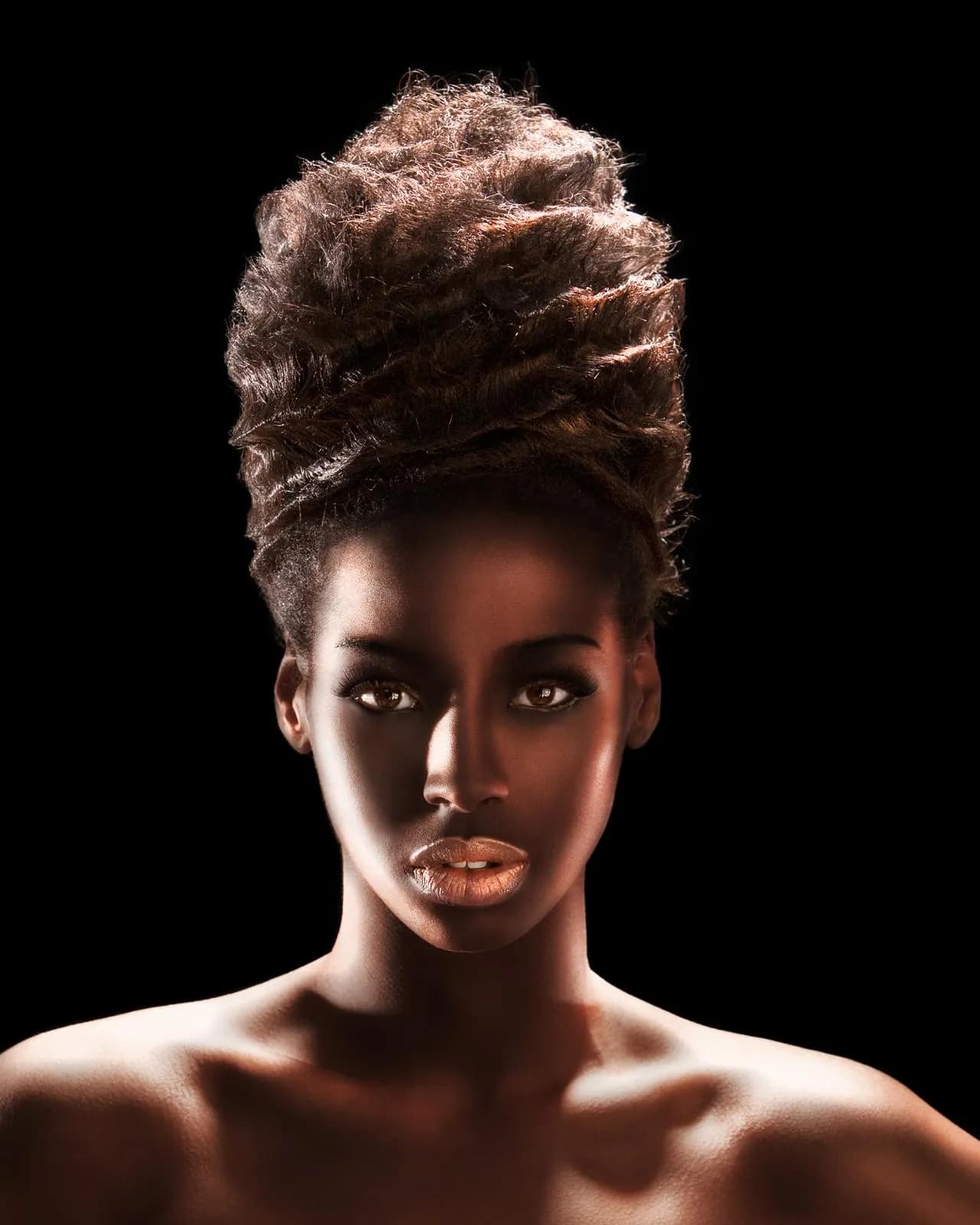 Model with a tall, textured updo, lit against a black background